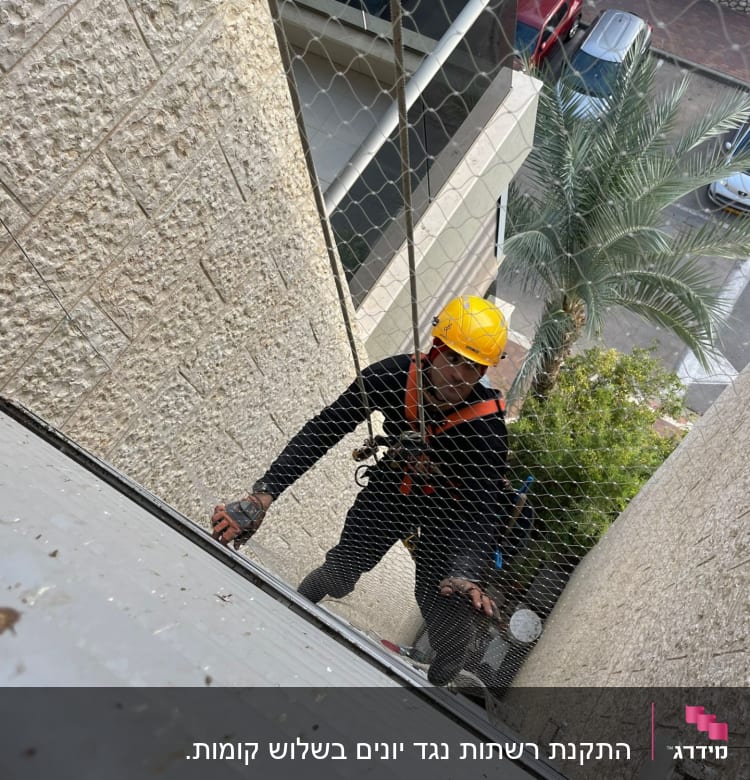 אדם עם קסדה צהובה מתקין רשת על קיר חיצוני